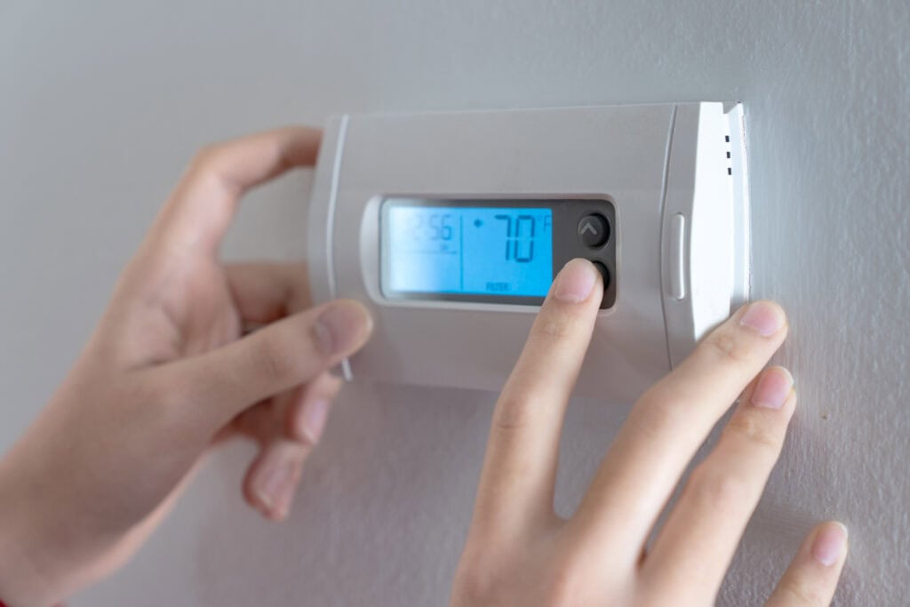 Adjusting a digital thermostat to 70 degrees.